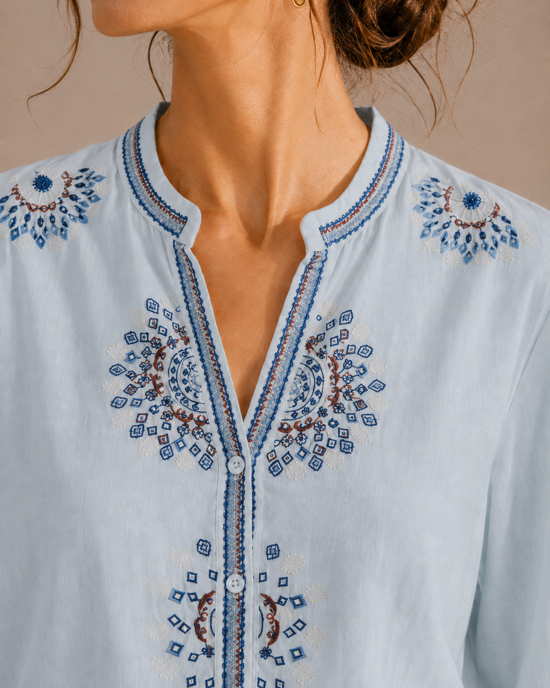 Close-up of the medallion embroidery around the neckline and front of the sky blue cotton shirt.
