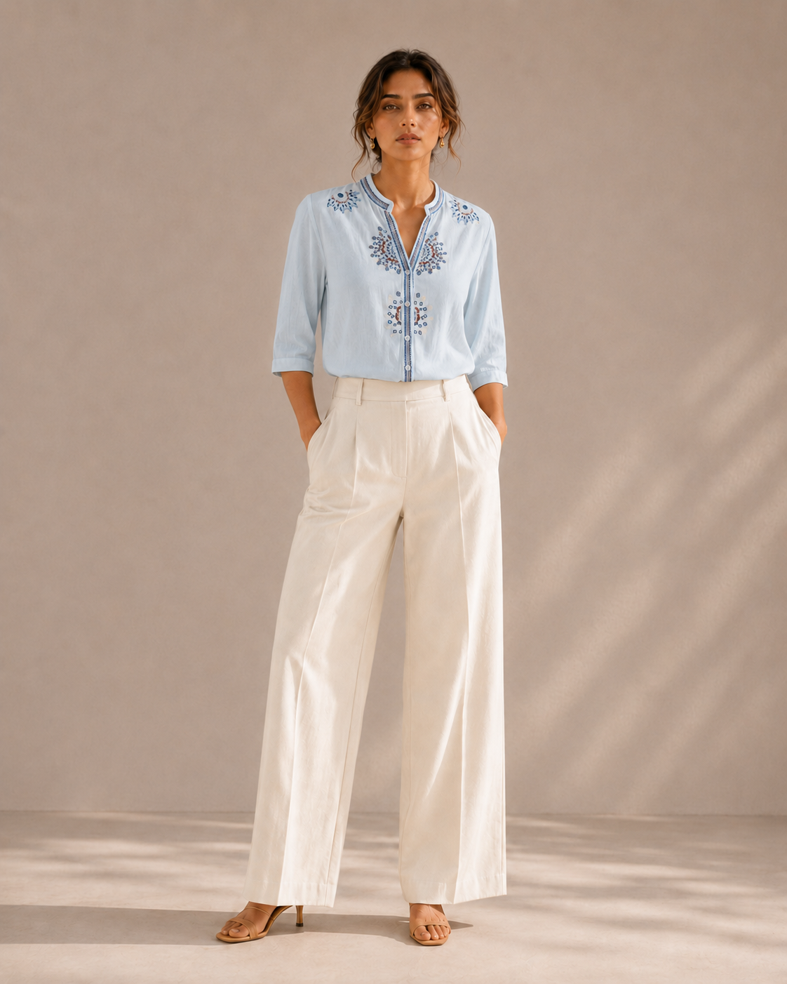 Full-length look of a woman wearing the sky blue medallion embroidered cotton shirt with light trousers.
