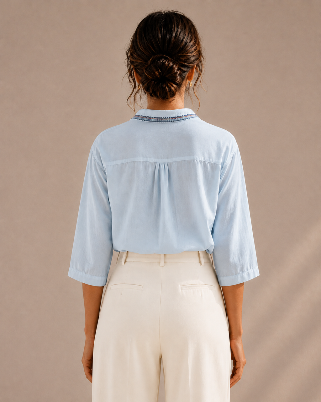 Back view of the sky blue medallion embroidered cotton shirt tucked into light trousers, showing the yoke and collar.
