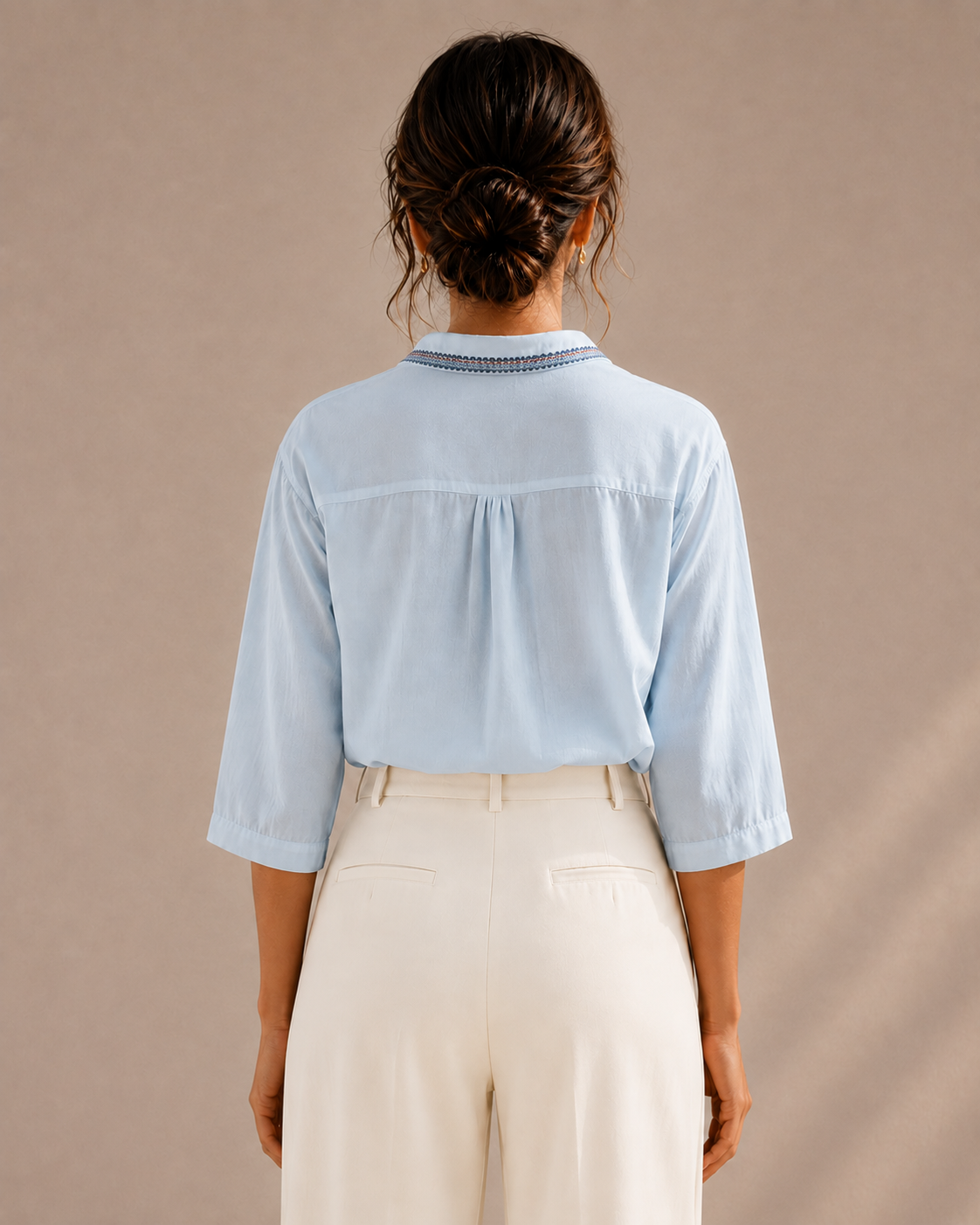 Back view of the sky blue medallion embroidered cotton shirt tucked into light trousers, showing the yoke and collar.
