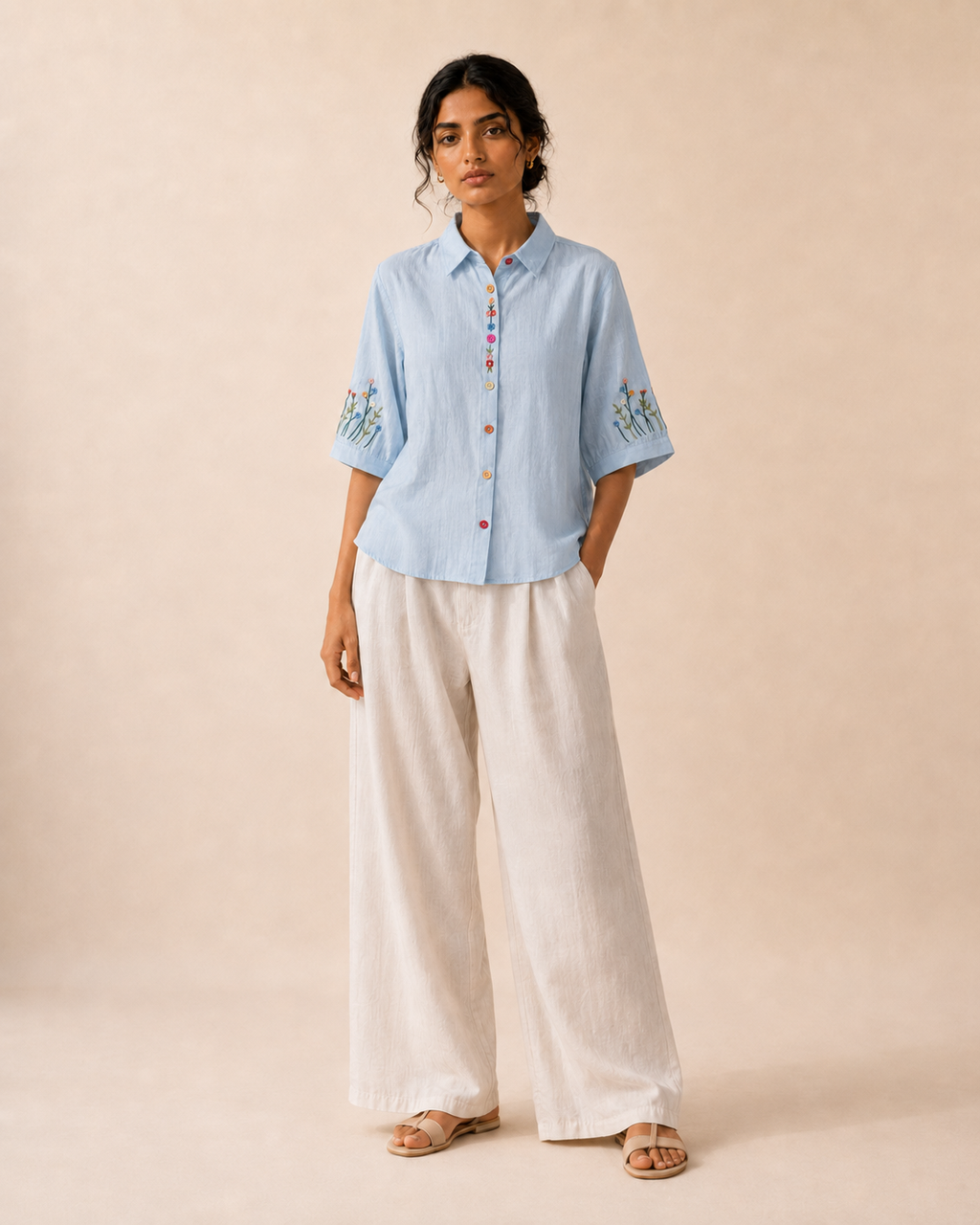 Full-length look of a woman wearing the sky blue wildflower embroidered cotton shirt with light trousers.
