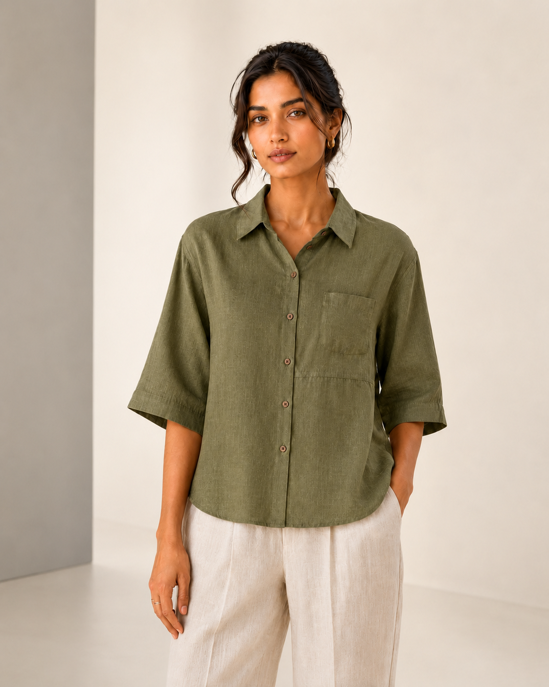 Studio front view of the olive green back embroidered embroidered linen shirt styled with light trousers.
