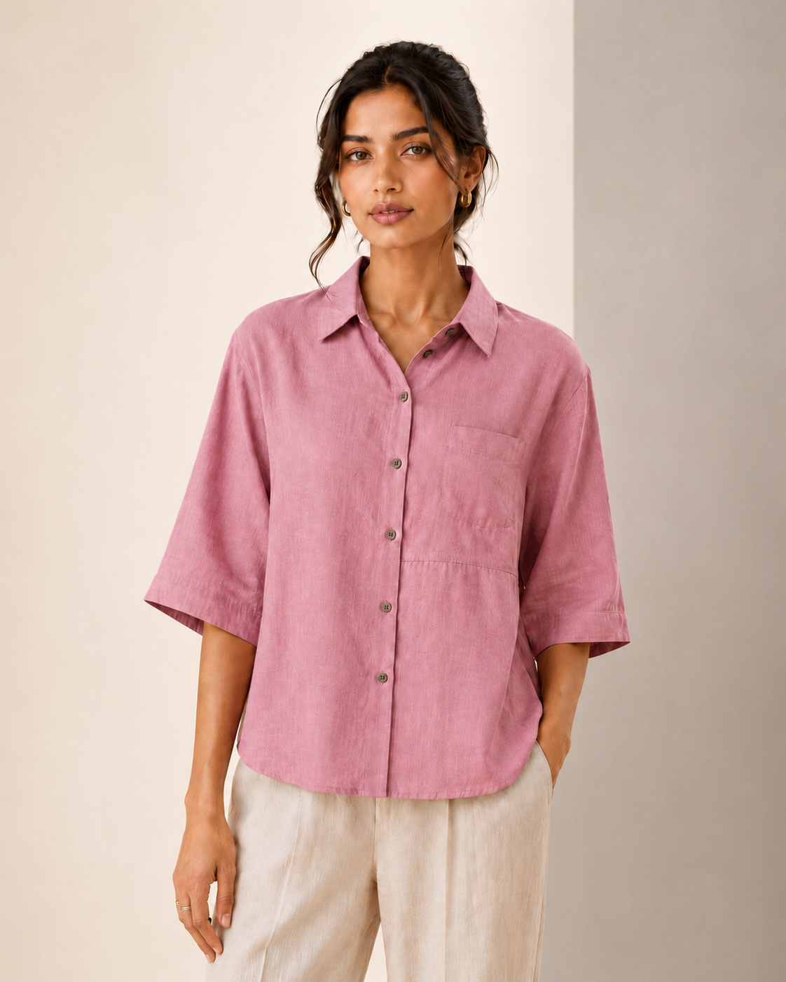 Studio front view of the soft blush pink back embroidered embroidered linen shirt styled with light trousers.
