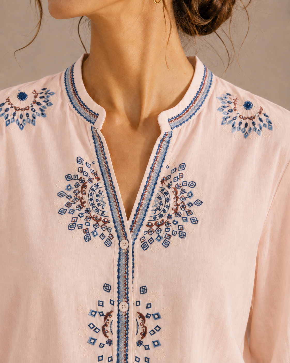 Close-up of the medallion embroidery around the neckline and front of the soft blush pink cotton shirt.
