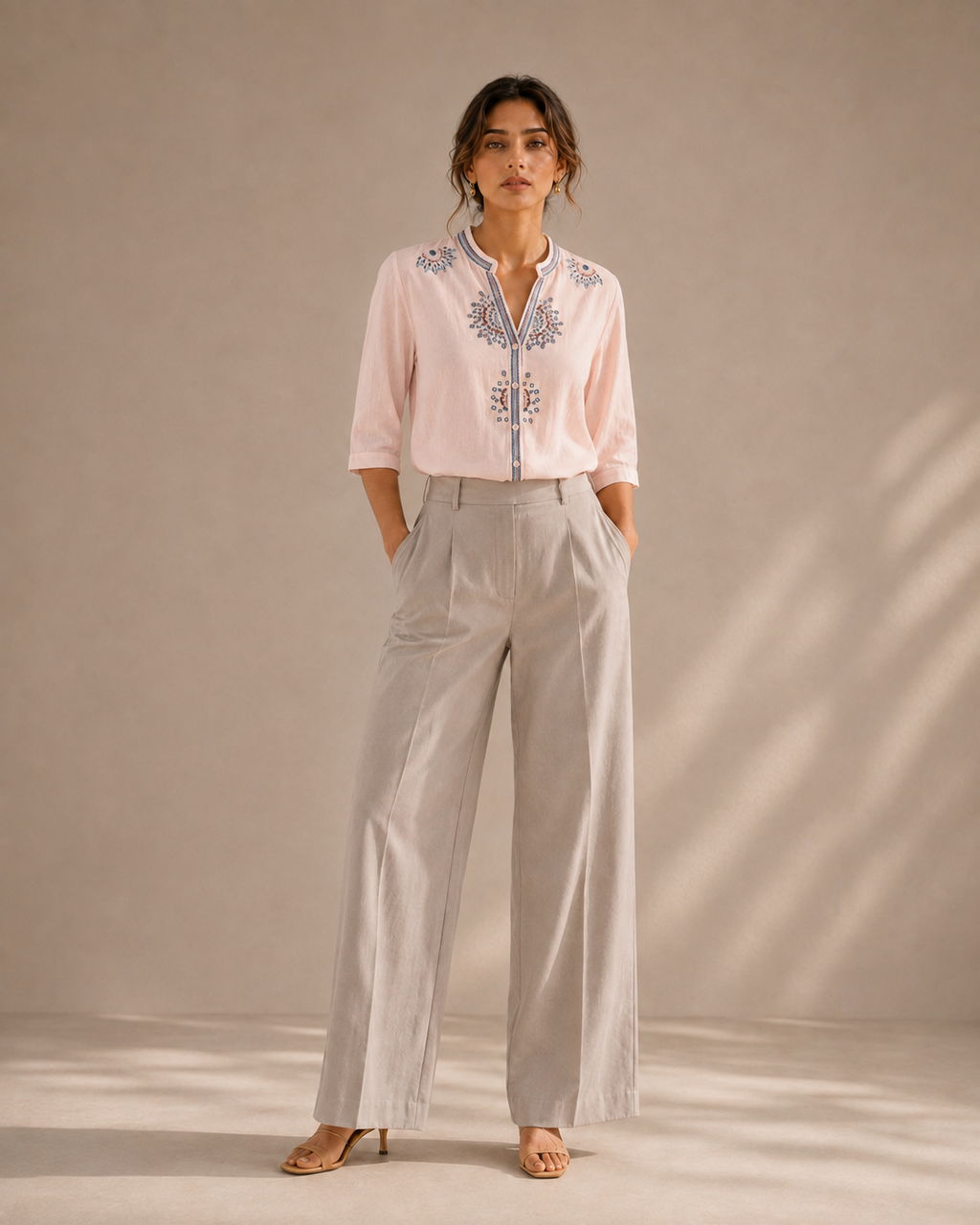 Full-length look of a woman wearing the soft blush pink medallion embroidered cotton shirt with light trousers.
