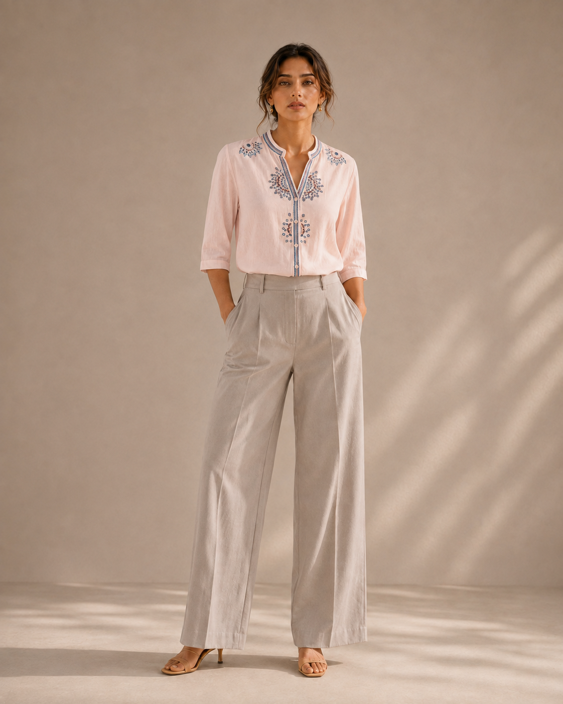 Full-length look of a woman wearing the soft blush pink medallion embroidered cotton shirt with light trousers.
