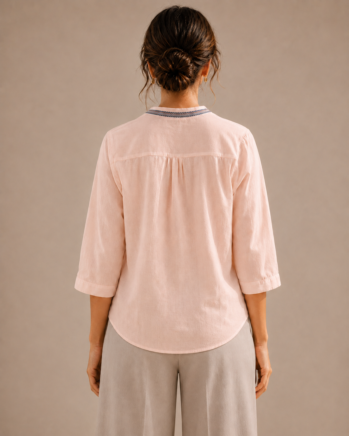 Back view of the untucked soft blush pink medallion embroidered cotton shirt, showing the curved hem and relaxed fit.
