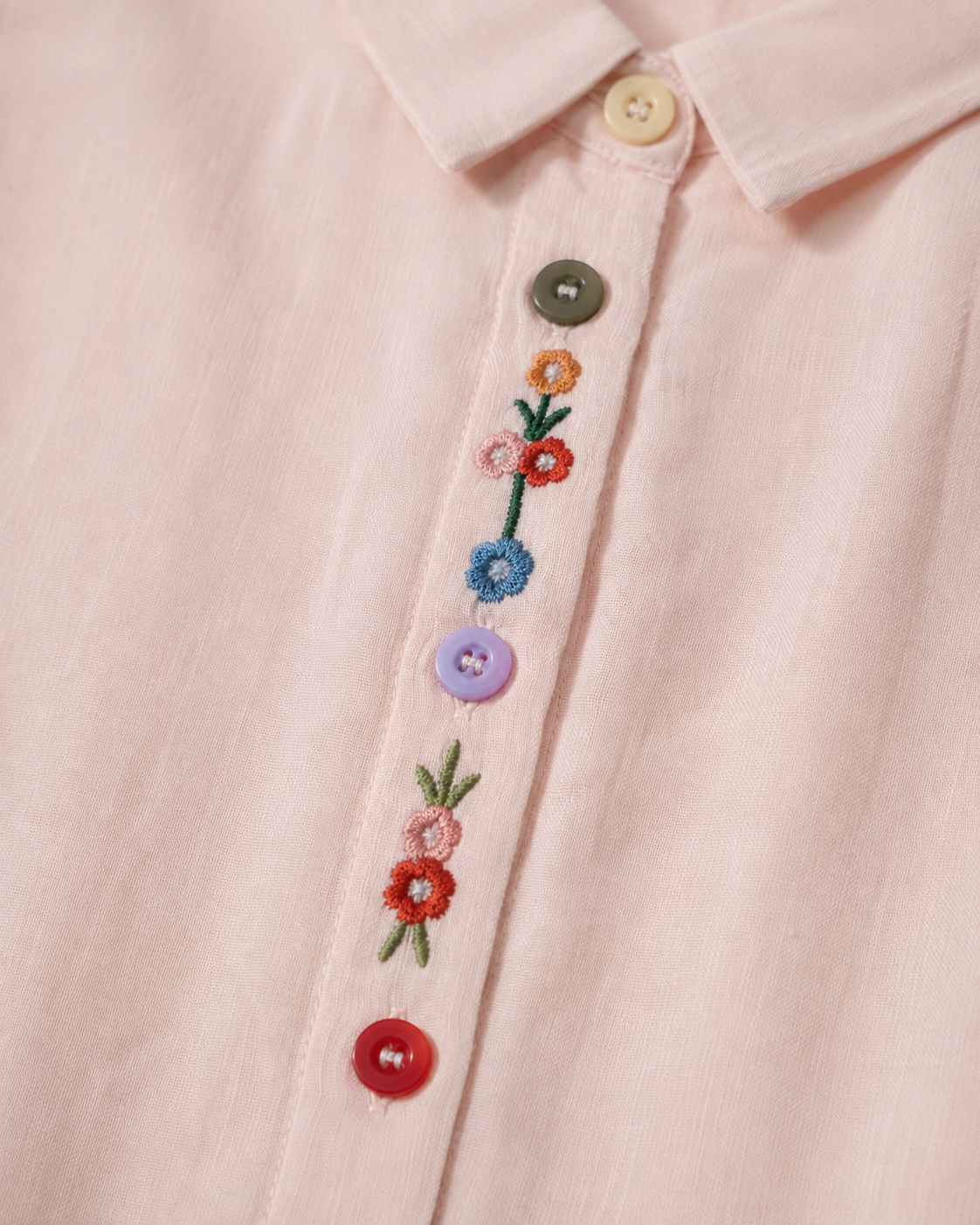 Close-up of wildflower embroidery and decorative buttons on the front placket of the soft blush pink cotton shirt.
