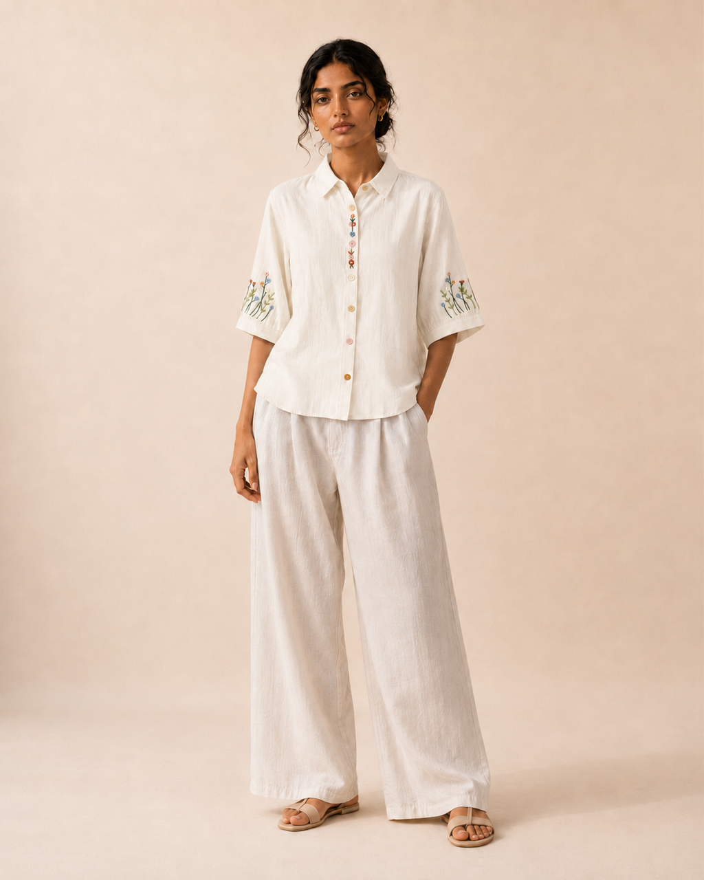 Full-length look of a woman wearing the ivory wildflower embroidered cotton shirt with light trousers.
