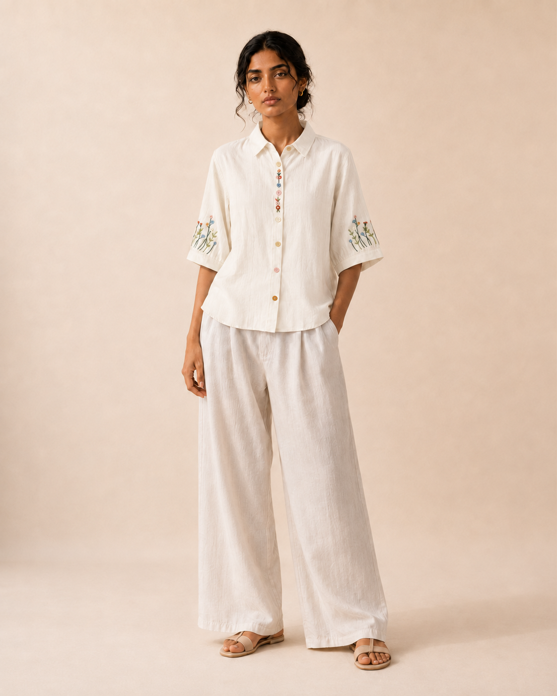 Full-length look of a woman wearing the ivory wildflower embroidered cotton shirt with light trousers.
