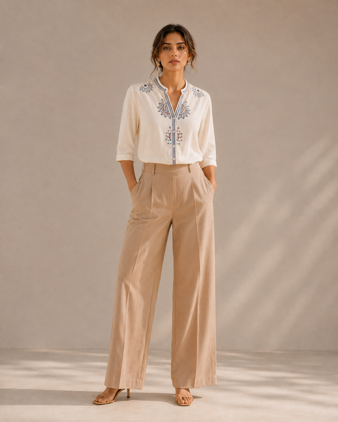 Full-length look of a woman wearing the warm ivory white medallion embroidered cotton shirt with light trousers.
