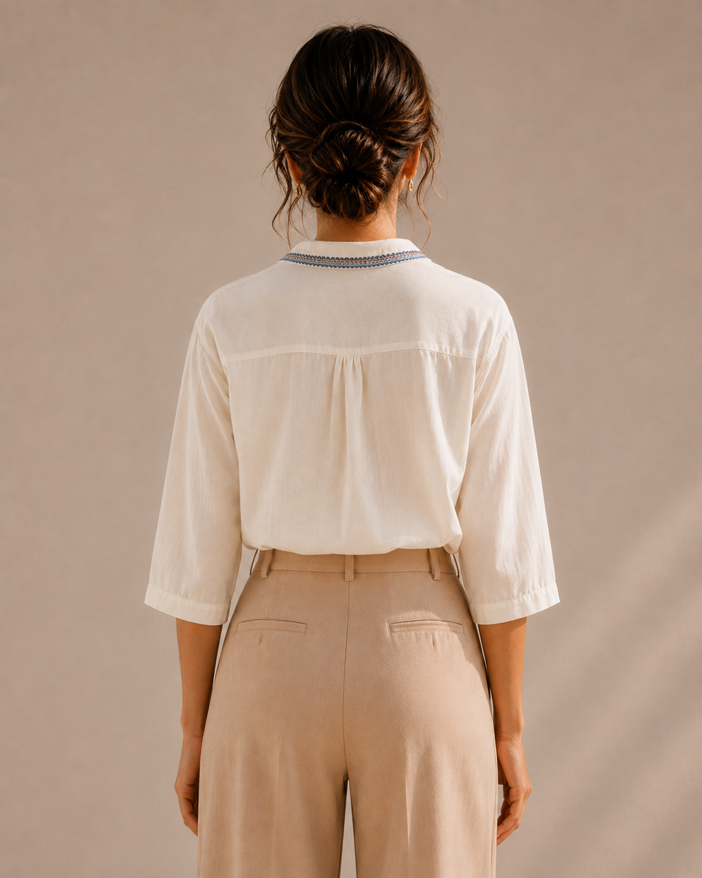 Back view of the warm ivory white medallion embroidered cotton shirt tucked into light trousers, showing the yoke and collar.
